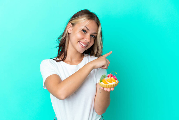 Young Russian woman holding a fruit sweet isolated on blue background pointing back - Photo, Image