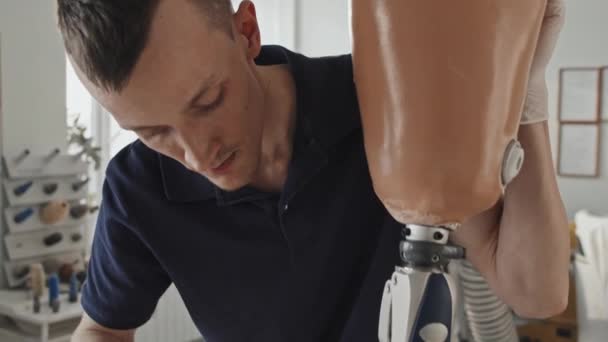 Tilt down shot of modern professional craftsman assembling and fixing parts of leg prosthesis in his workshop - Metraje, vídeo