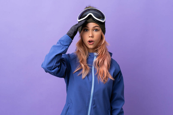 Skier adolescente avec des lunettes de snowboard sur fond violet isolé a réalisé quelque chose et l'intention de la solution - Photo, image