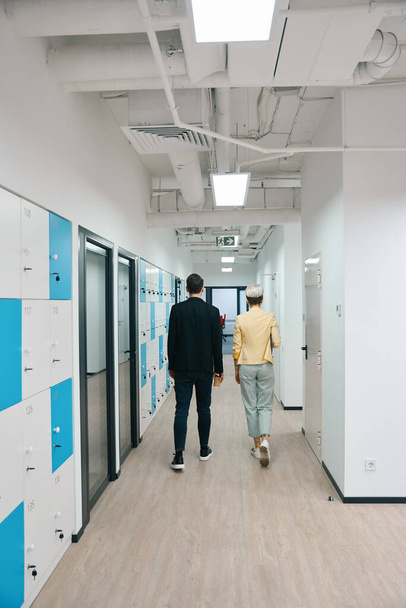 Colleagues walking along bright illuminated hall with storage cells to their office, coworking space - Foto, afbeelding