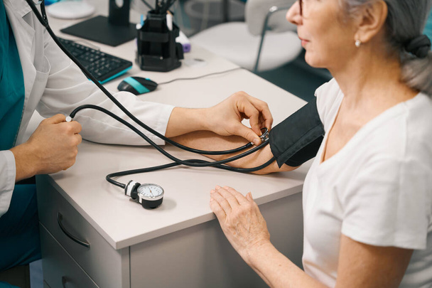 Therapist measures the blood pressure of a pensioner, the doctor uses a tonometer and a stethoscope - Fotó, kép