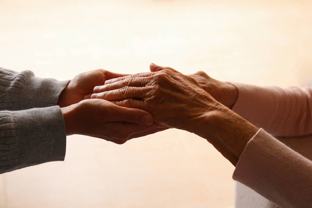 Cropped studio shot of elderly woman and female geriatric social worker holding hands. Women of different age comforting each other. Close up, background, copy space. - Foto, immagini