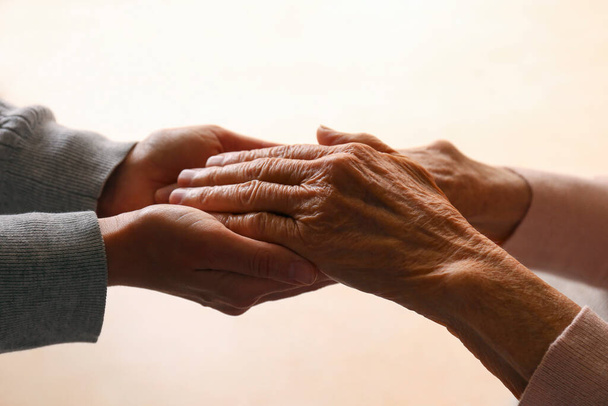 Cropped studio shot of elderly woman and female geriatric social worker holding hands. Women of different age comforting each other. Close up, background, copy space. - 写真・画像