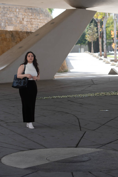 Молодая привлекательная женщина в повседневной одежде и с сумочкой в руках гуляет по городу. - Фото, изображение
