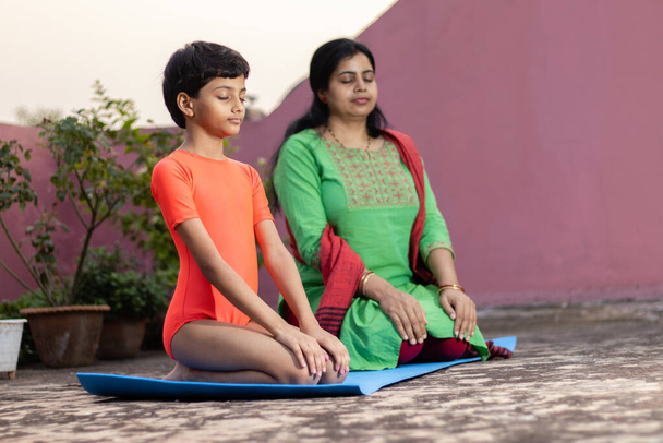 Uma criança menina indiana com a mãe praticando Vajrasana ioga no tapete de ioga ao ar livre - Foto, Imagem