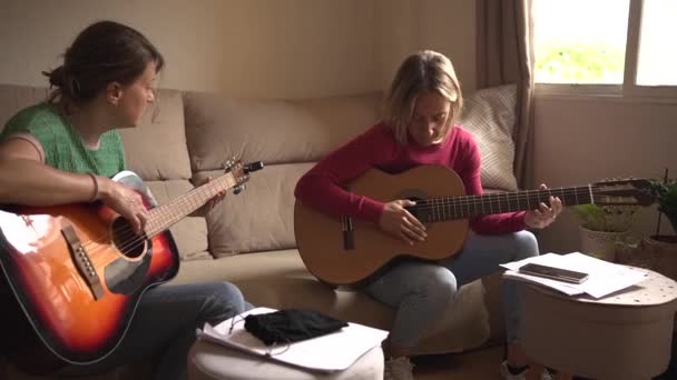 Zwei Frauen in den Vierzigern üben auf dem Sofa Gitarre, stimmen ihre Gitarren mit einem Stimmgerät und einem Handy. Klassik und Akustik  - Filmmaterial, Video