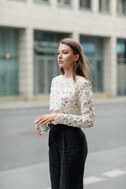 Fashionable young and fair haired woman in white lace top and pants holding coffee to go   - Photo, Image