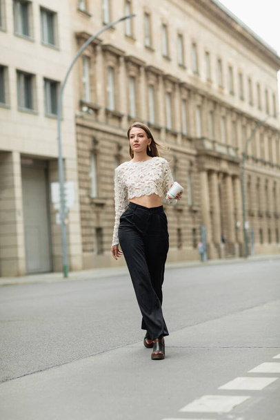 young woman in lace top and high waist pants holding coffee to go on street in Berlin, Germany  - Photo, Image