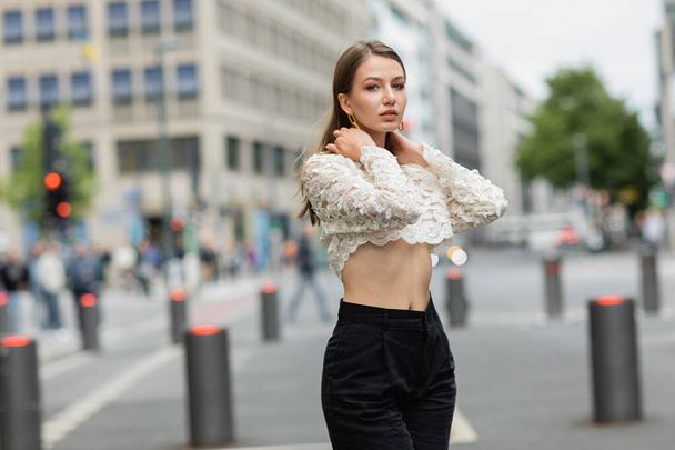 Hübsche junge Frau posiert in Spitzenoberteil und Hose mit hoher Taille auf der Straße in Berlin - Foto, Bild