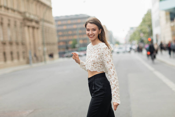 Cheerful young woman in lace top and high waist pants walking on street in Berlin, Germany  - Photo, Image