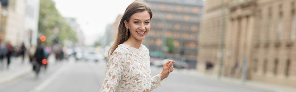 Cheerful young woman in lace top and high waist pants walking on street in Berlin, Germany banner - Photo, Image