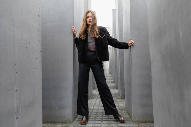 Stilvolle junge Frau in Jacke steht zwischen dem Denkmal für die ermordeten Juden Europas in Berlin - Foto, Bild
