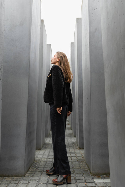 egy fekete kabátos nő félrenéz, miközben a meggyilkolt európai zsidók emlékműve között áll.  - Fotó, kép