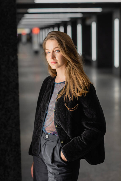 attraktive junge Frau in schwarzer Jacke posiert in modernem Gebäude mit Leuchtstoffröhren in Berlin - Foto, Bild