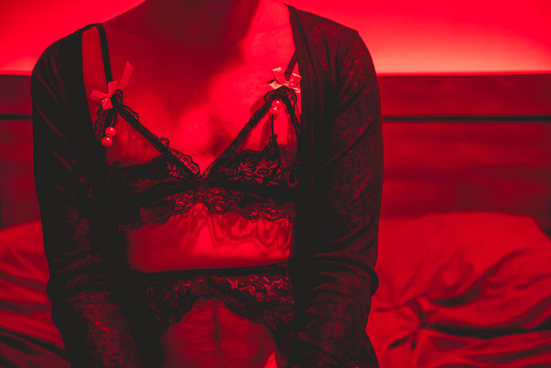 Taivutus sukupuolinormit: sängyssä ei-binary femboy viettelevä musta alusvaatteita ja intohimoinen punainen valo - Valokuva, kuva