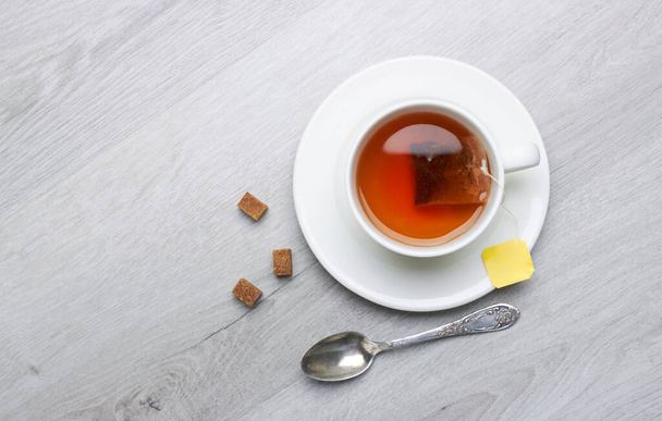 Чашка чая и пакетиков, ложка, сахар, на светлом деревянном фоне - Фото, изображение