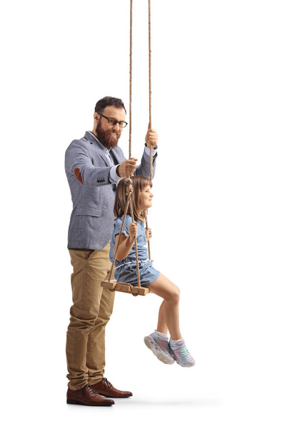 Full length profile shot of a man standing behind a girl on a swing isolated on white background - Foto, imagen