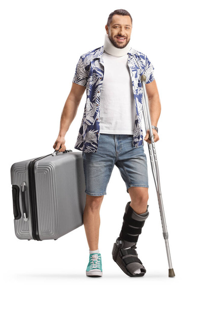 Male passenger with an orthopedic boot and cervical collar standing with a crutch and holding a suitcase isolated on white background - Foto, Imagen