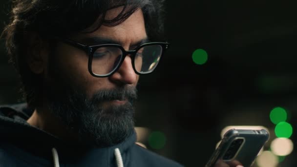 Close-up Indiase man met baard in glazen op donkere parkeerplaats ondergrondse avond met behulp van mobiele telefoon app chatten sociale media online Arabische man Moslim man typen browsen smartphone boeking taxi - Video