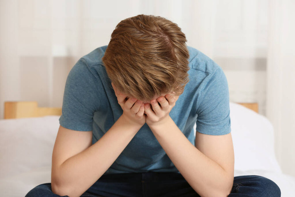 Unhappy teenage boy covering face with hands on bed at home - Foto, Bild