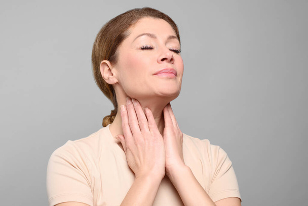 Woman suffering from sore throat on light grey background - Foto, afbeelding