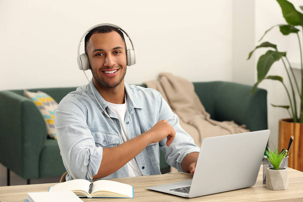 Portrait of African American man in headphones near laptop at wooden table in room - Foto, Imagem
