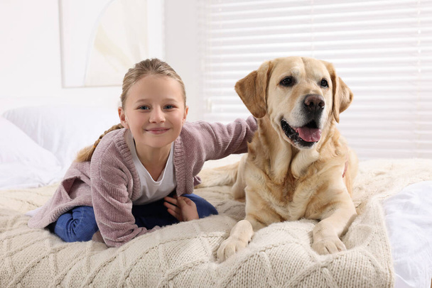 Cute child with her Labrador Retriever on bed at home. Adorable pet - Fotoğraf, Görsel