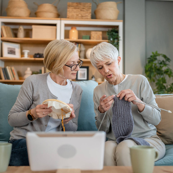 two women senior mature caucasian friends or mother and daughter or sisters knitting and embroidery during leisure time at home needlework concept happy and relaxed enjoy free time - Photo, image