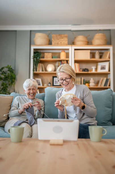 two women senior mature caucasian friends or mother and daughter or sisters knitting and embroidery during leisure time at home needlework concept happy and relaxed enjoy free time - Photo, Image