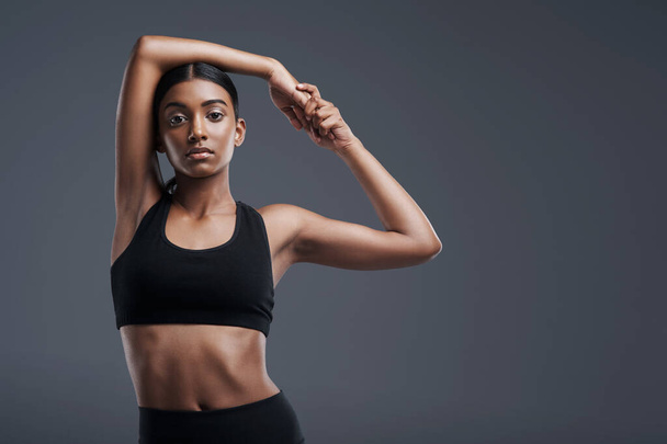 Portrait, mockup and stretch with a sporty woman in studio on a gray background for fitness or health. Exercise, workout and warm up with a young focused indian female athlete training her body. - Foto, imagen
