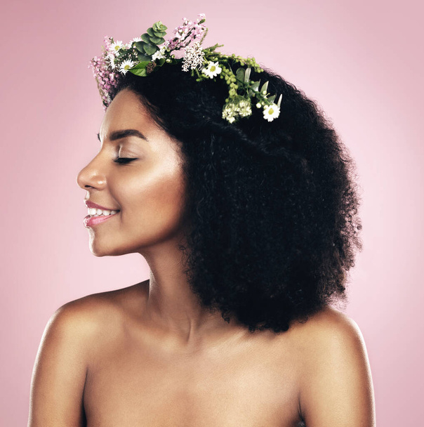 Happy woman, face and flower crown for beauty in studio, pink background and natural skincare. Smile, african model and plants for floral wreath, spring cosmetics and dermatology of afro hair care. - Photo, Image