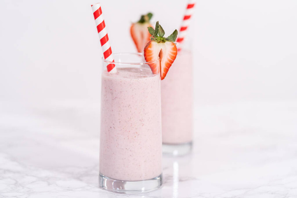 Freshly made healthy breakfast strawberry banana smoothie garnished with fresh strawberry and paper straw. - Zdjęcie, obraz