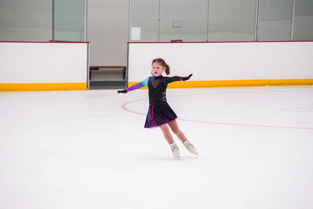 Klein meisje oefenen voor haar kunstschaatsen competitie op de indoor ijsbaan. - Foto, afbeelding