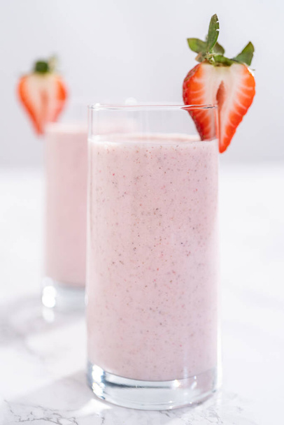Freshly made healthy breakfast strawberry banana smoothie garnished with fresh strawberry and paper straw. - Fotoğraf, Görsel