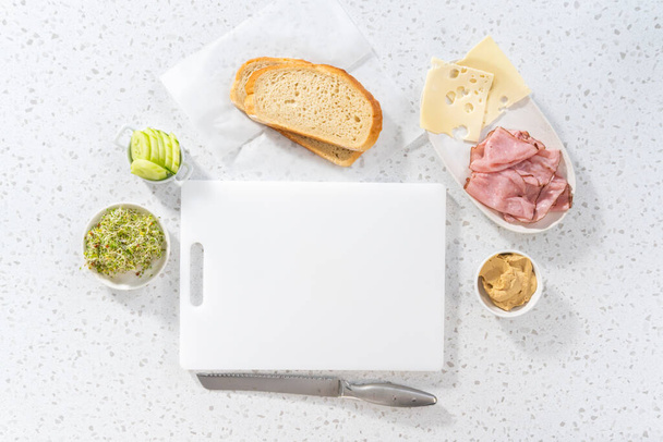 平置きだ。白いまな板にハム、キュウリ、もやしのサンドイッチを組み立てます。. - 写真・画像