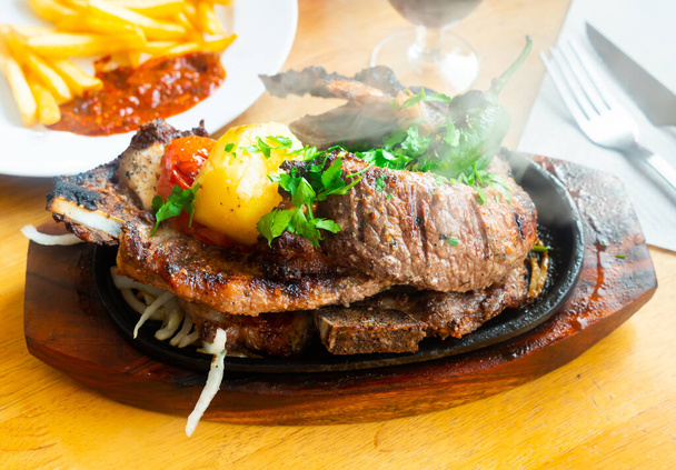 Appetizing beef ribs with baked potato slices and vegetables served on platter - Photo, Image