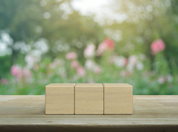 Three block cubes on wooden table over blur pink flower and tree in garden - Zdjęcie, obraz