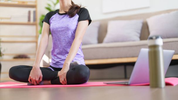 Спортивная женщина медитирует и дышит, чтобы практиковать йогу упражнения во время изучения йоги онлайн дома. - Фото, изображение