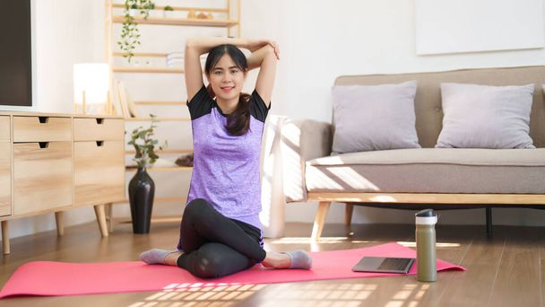 Sportos nő ül a szőnyegen nyújtózkodó könyök és a váll után gyakorló jóga otthon. - Fotó, kép