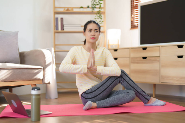 Sportos nő néz jóga edzés online és jóga csinál namaste pózt és csavar gyakorlat. - Fotó, kép