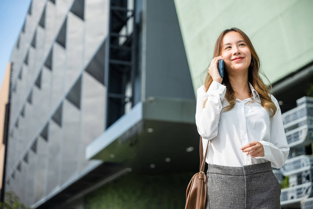 Beautiful young Asian woman calling and talks on telephone or mobile phone in city, Portrait of businesswoman smiling talking on mobile phone, people and technology communication concept - Foto, Imagen