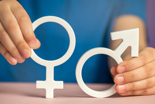 The concept of gender equality. Symbol of female and male gender in hand as a symbol of equality of rights. On a purple background in a blue t-shirt with copy space. High quality photo - Photo, Image