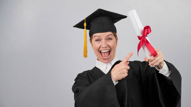 Happy woman in graduate gown pointing finger at received diploma - Foto, immagini