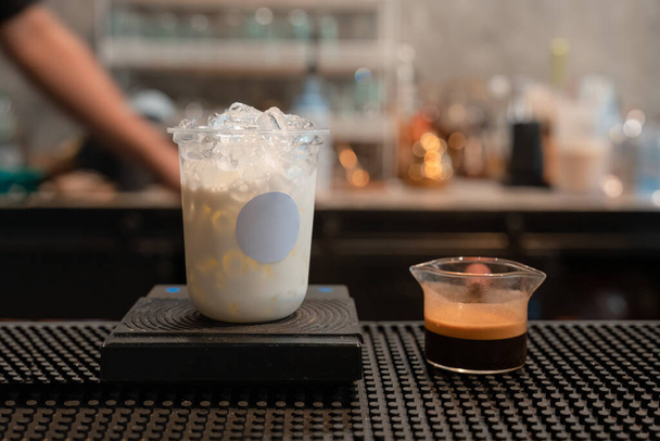 Bicchiere di latte con ghiaccio e caffè espresso da miscelare come caffelatte sul bancone della caffetteria - Foto, immagini