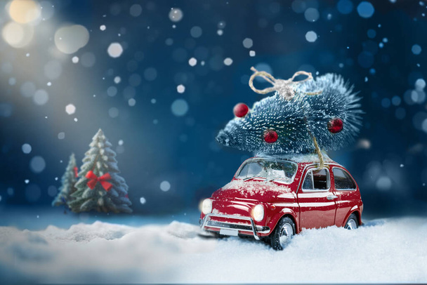 Retro toy car carrying christmas tree on roof in snowy winter forest. Christmas night background. Holidays card - Fotoğraf, Görsel
