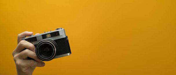 Image of hand holding vintage camera isolated on yellow background. Empty space for your advertising. - Photo, Image