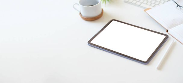 Digitales Tablet mit leerem Bildschirm auf Kaffeetasse und Notizblock auf weißem Schreibtisch. Kopieren Sie Platz für Ihren Text. - Foto, Bild