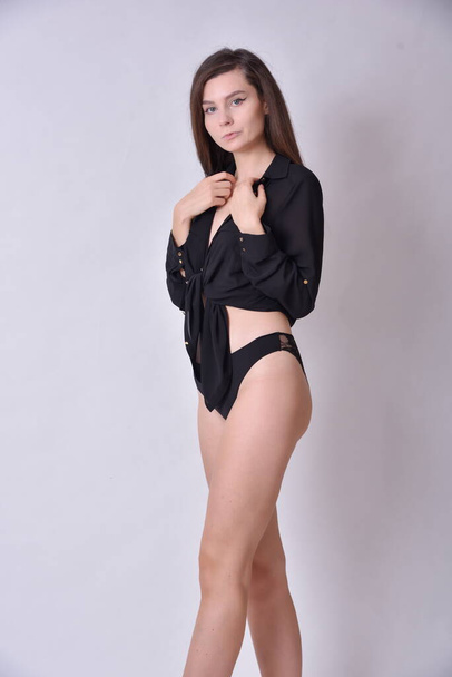 Junge Frau, brünett. Weibliches Modell mit schwarzem Oberteil und schwarzer Unterwäsche. Weißer Hintergrund, Studiofoto. - Foto, Bild