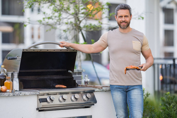 Barbecue concept. Middle aged hispanic man in t-shirt for barbecue. Roasting and grilling food. Roasting meat outdoors. Barbecue and grill. Cooking meat in backyard - Fotoğraf, Görsel