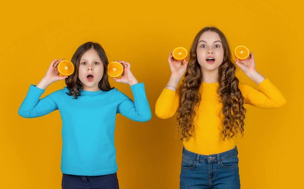 amazed teen children hold orange fruit on yellow background. - 写真・画像